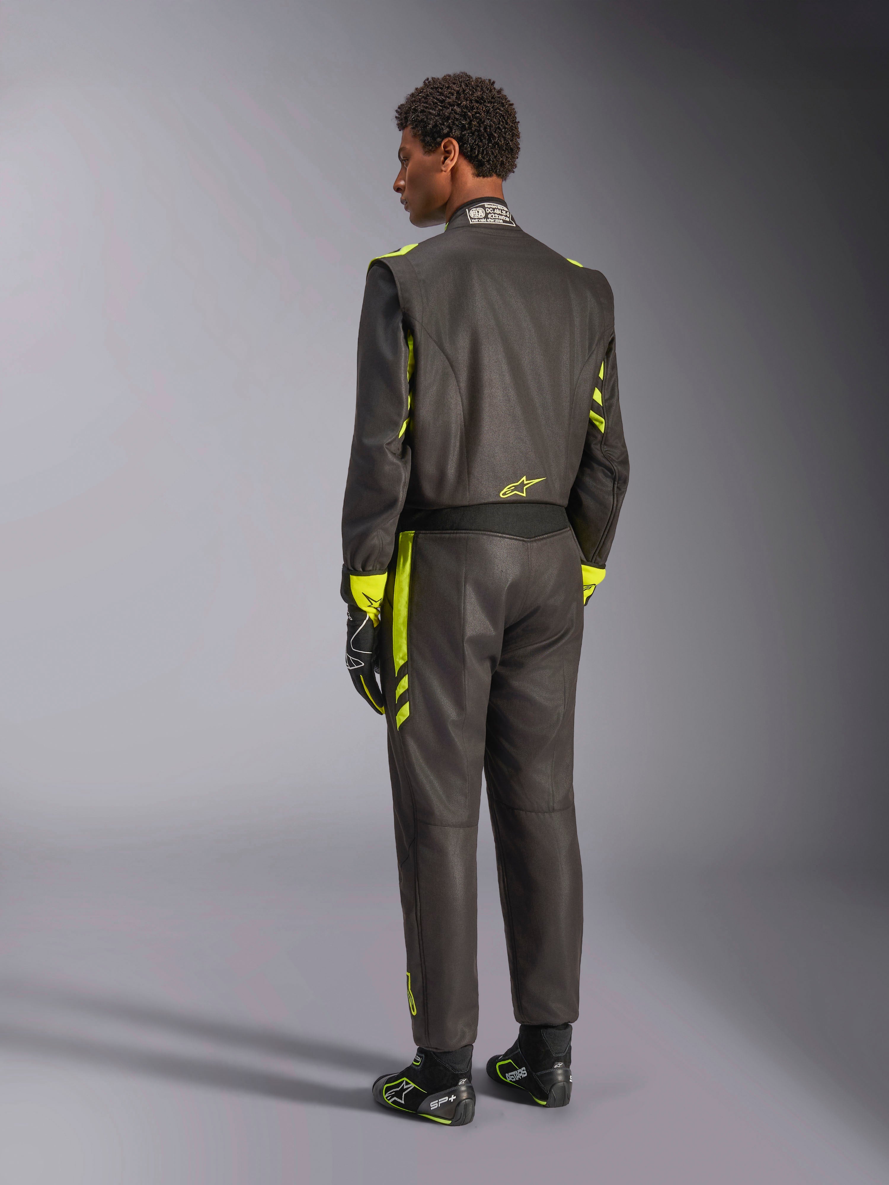 Vista traseira do Fato Alpinestars GP Race V3 FIA, preto com detalhes em amarelo fluo, usado com luvas e botas de corrida a condizer, equipamento profissional de automobilismo com uma construção de duas camadas em aramida