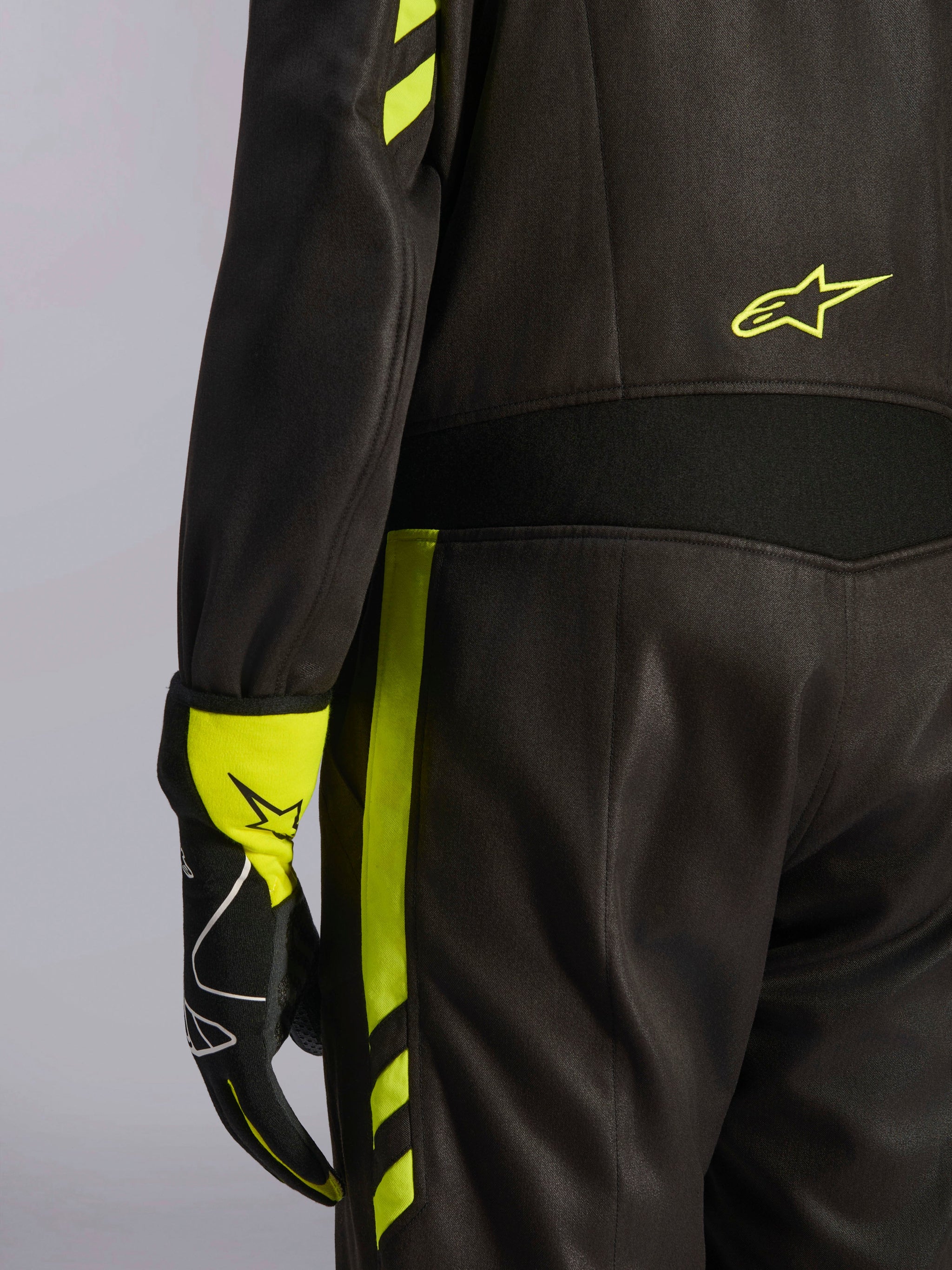 Alpinestars GP Race V3 Suit FIA, preto e amarelo fluo, detalhe em grande plano da cintura e da lateral da perna, com painéis elásticos de aramida e luva de corrida a condizer, equipamento profissional de automobilismo