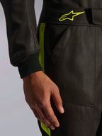 Fato Alpinestars GP Race V3 FIA, fato de automobilismo, preto e amarelo fluo, vista de pormenor que mostra a cintura ajustável com logótipo de estrela amarela, punho da manga canelado e detalhe de risca lateral, equipamento profissional de automobilismo.