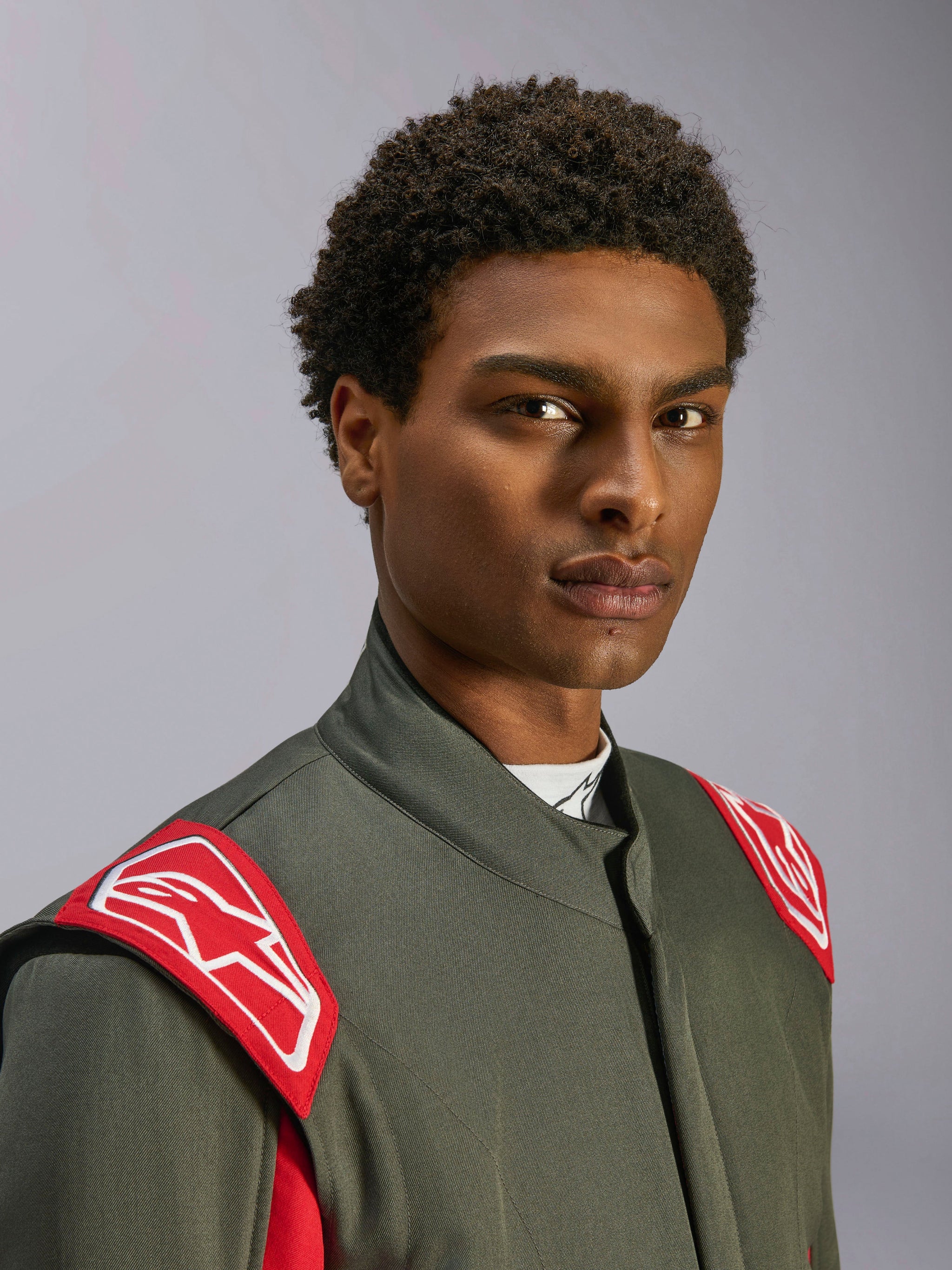 Alpinestars GP Race V3 Suit FIA, fato de automobilismo, antracite e vermelho, grande plano do tronco superior e cabeça, apresentando dragonas vermelhas nos ombros com o logótipo Alpinestars branco, gola alta e material de sarja cinzenta