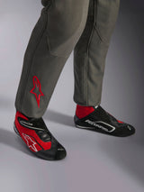 Alpinestars GP Race V3 Suit FIA, fato de corrida Antracite e Vermelho, pormenor da parte inferior das pernas com logótipo de estrela bordado a vermelho, combinado com botas de corrida vermelhas e pretas, equipamento automóvel profissional concebido para a proteção e o conforto do piloto