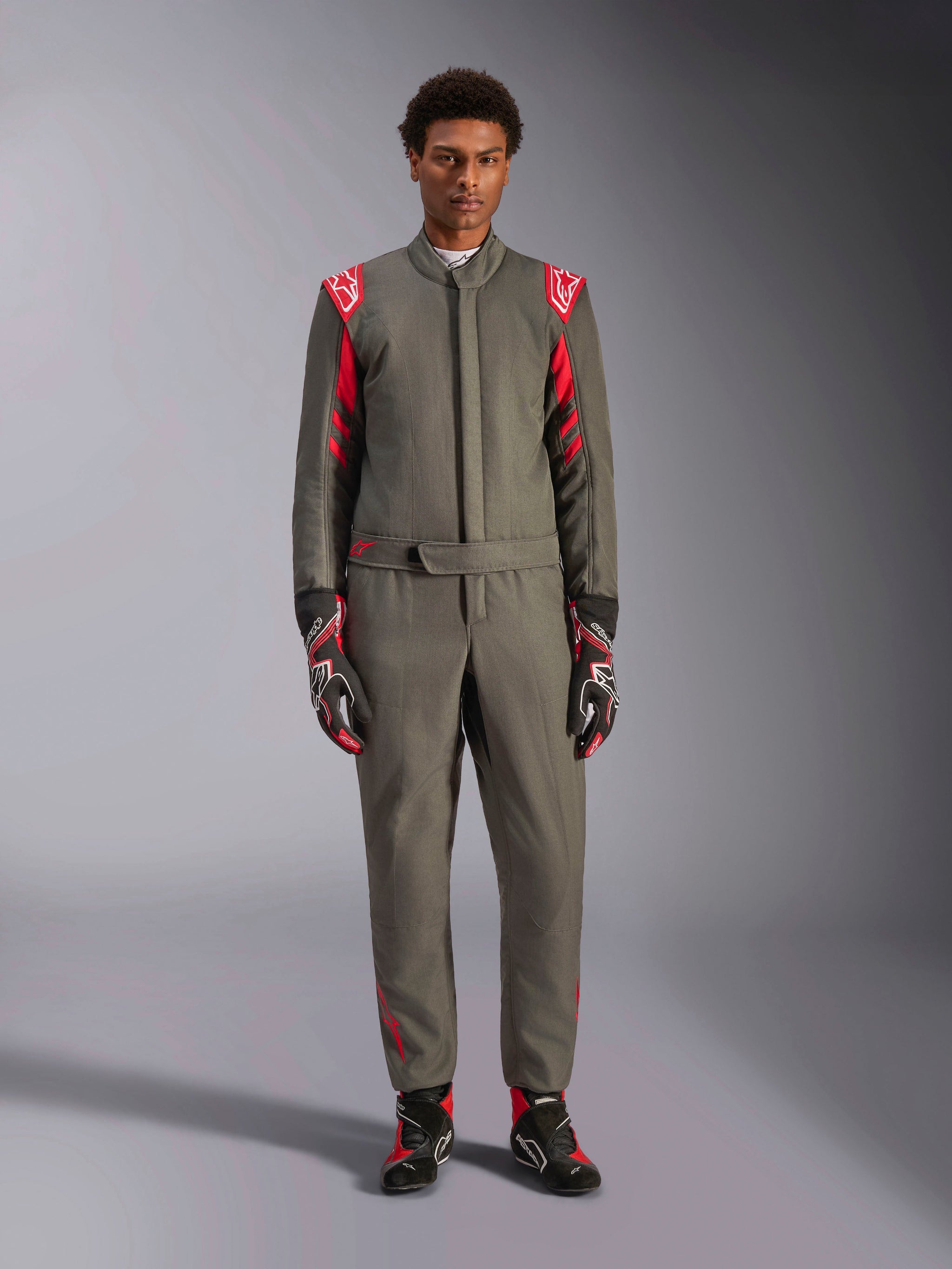 Alpinestars GP Race V3 Suit FIA, fato de automobilismo, antracite e vermelho, usado por um modelo masculino com luvas e botas a condizer, com dragonas vermelhas nos ombros e logótipos da marca, equipamento profissional de desportos motorizados para condução de alta performance
