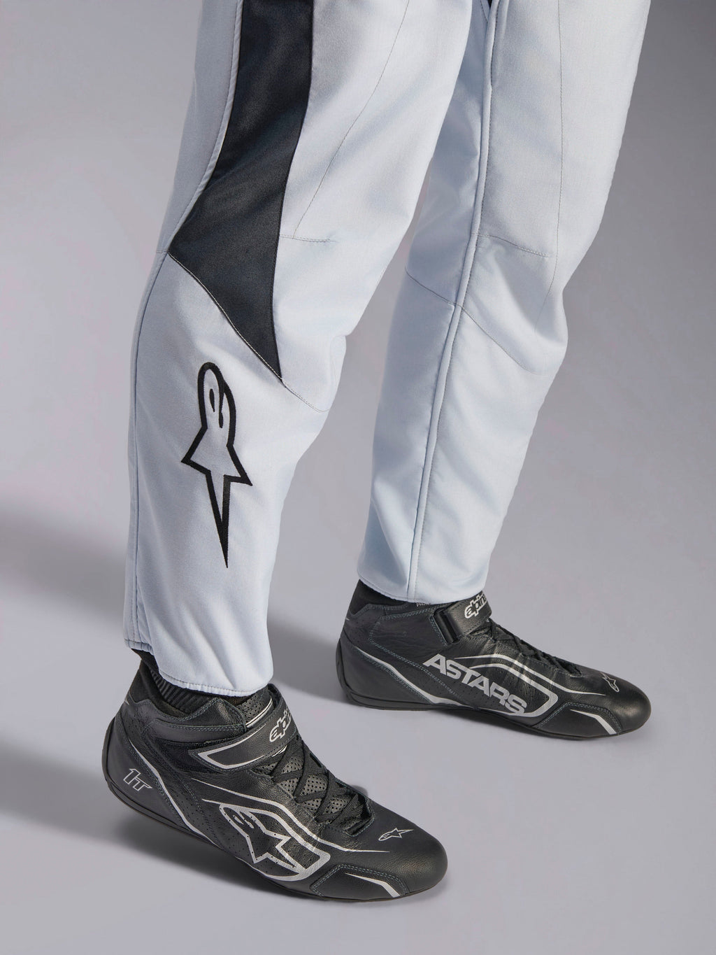 Alpinestars GP Pro Comp V2 FIA, macacão de automobilismo cinzento e preto, pormenor das pernas com logótipo e botas racing.