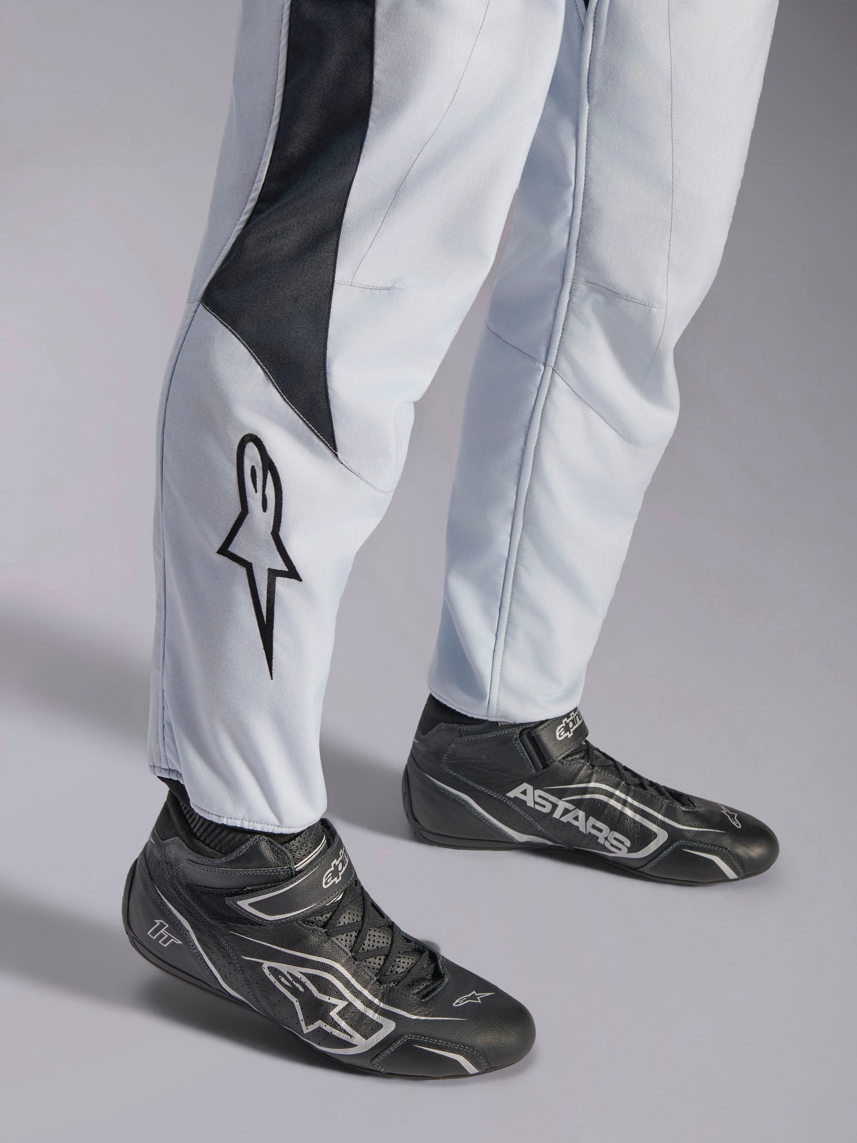 Alpinestars GP Pro Comp V2 FIA, macacão de automobilismo cinzento e preto, pormenor das pernas com logótipo e botas racing.