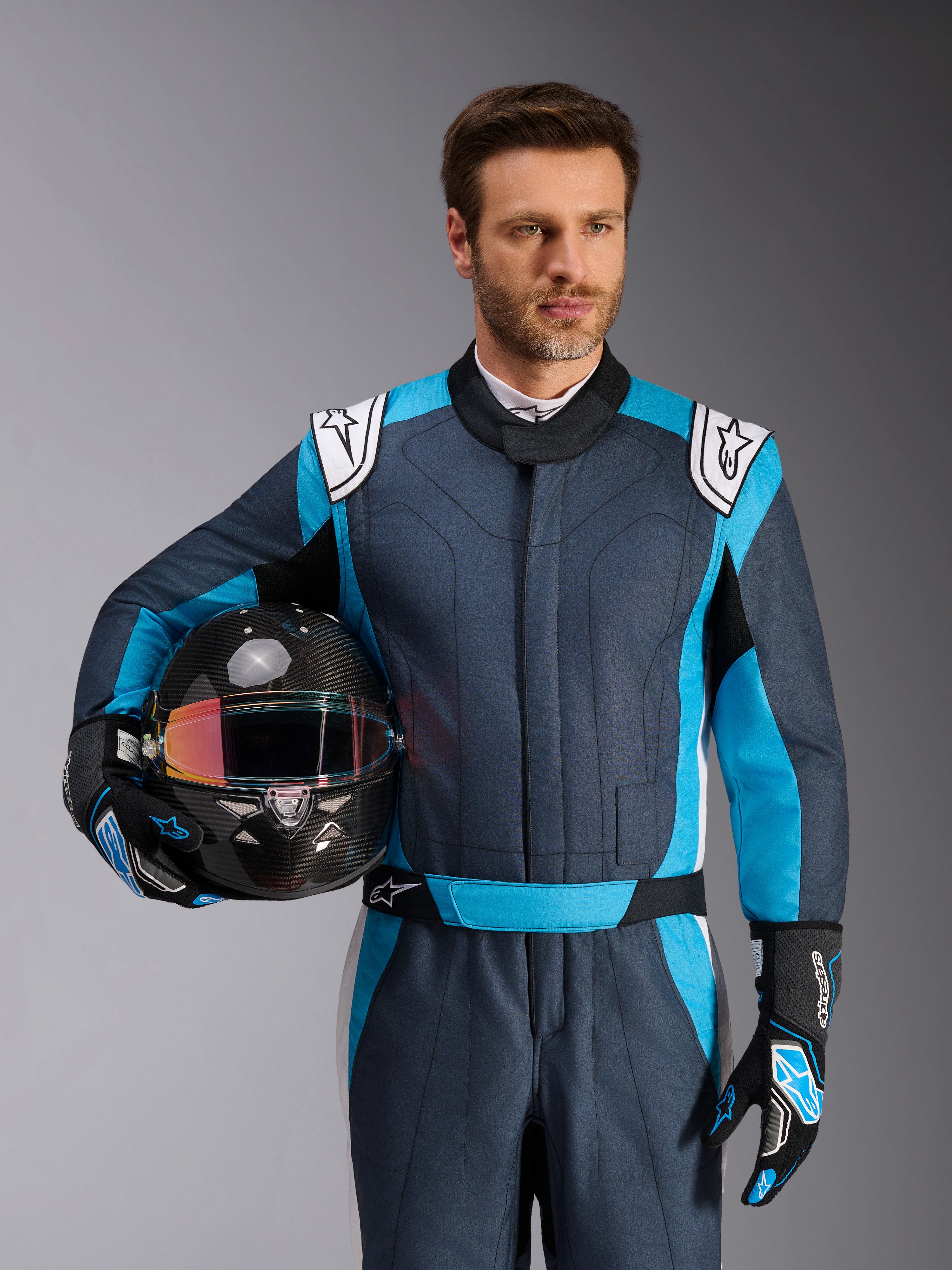 Alpinestars Macacão GP Pro Comp V2 - FIA, fato de corrida masculino, ciano e branco, piloto a segurar um capacete.