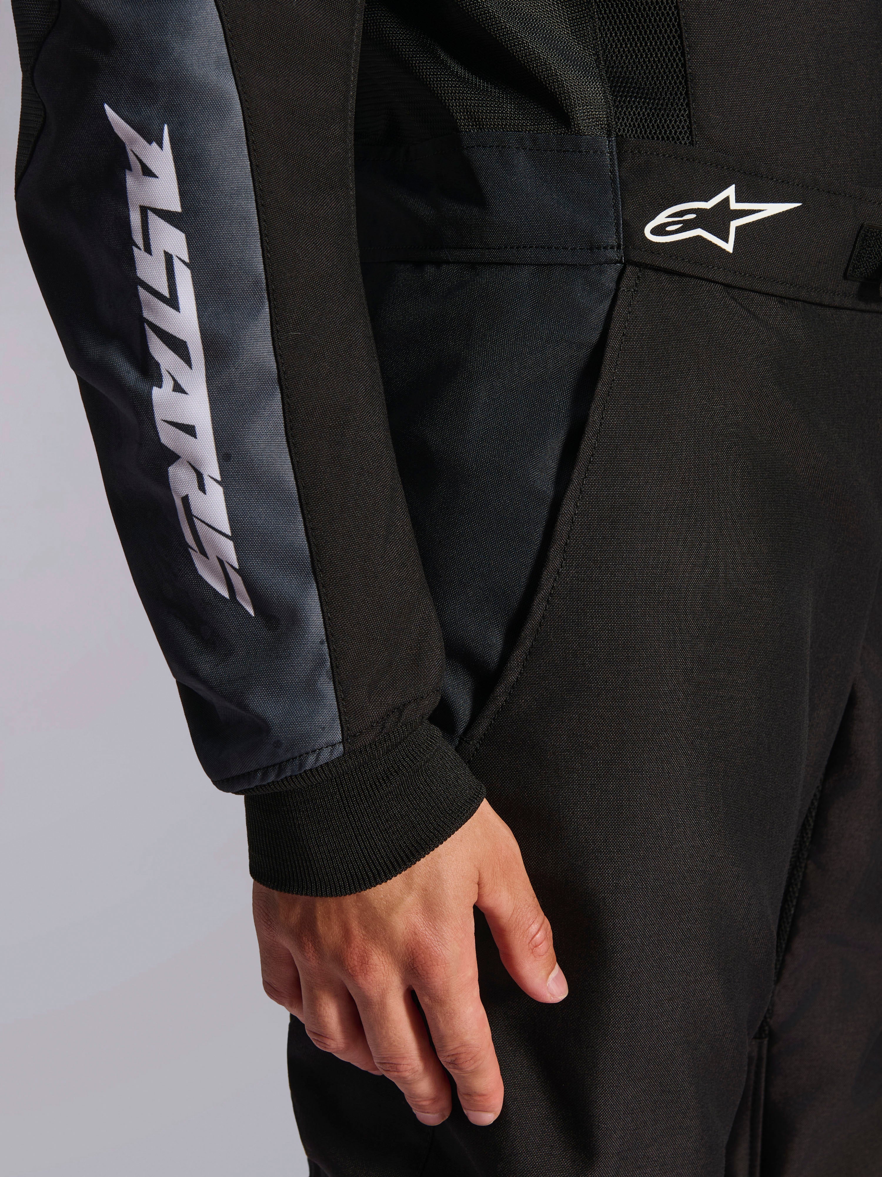 Macacão Alpinestars KMX-5 V3, macacão de karting, preto e Dark Shadow, pormenor em grande plano da anca e do braço, marca ASTARS branca na manga, logótipo branco na cintura, painéis de malha para ventilação e punho de malha