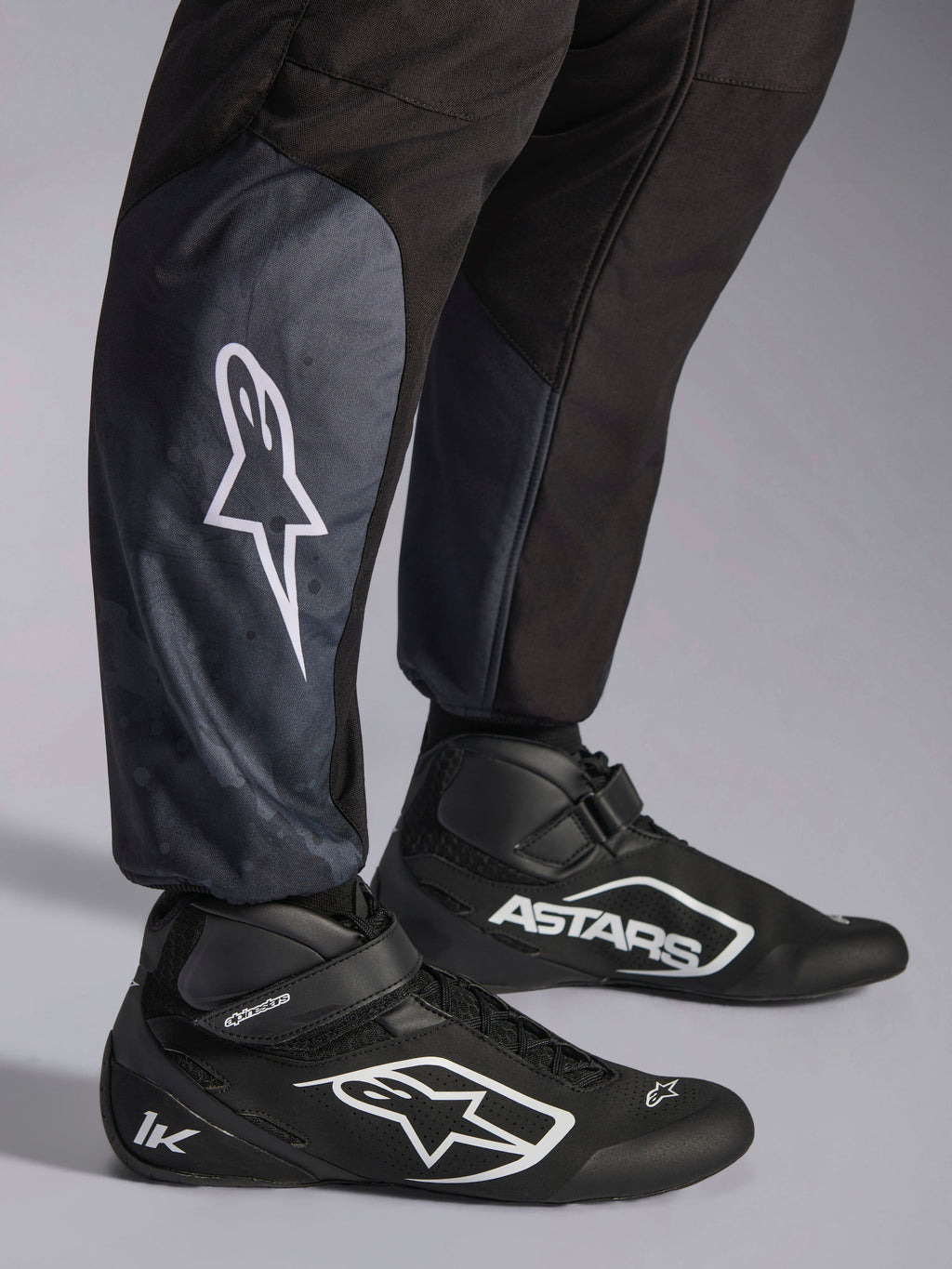 Macacão Alpinestars KMX-5 V3, Preto, grande plano da parte inferior das pernas e tornozelos, logótipo de estrela branco na perna, combinado com sapatos de karting pretos, destacando os punhos de malha nos tornozelos e o corte atlético-regular
