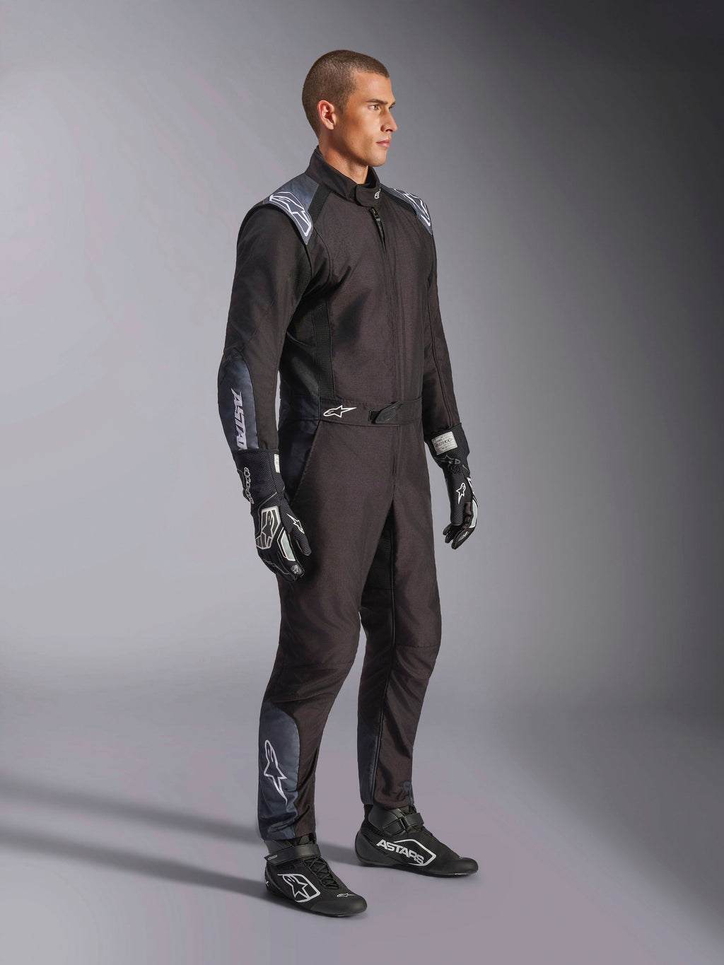 Macacão Alpinestars KMX-5 V3, fato de karting em Black Dark Shadow, usado com luvas e botas de corrida pretas a condizer, com perfurações cortadas a laser e painéis de malha tecnológica, design elegante de camada dupla com logótipos brancos para desporto motorizado profissional
