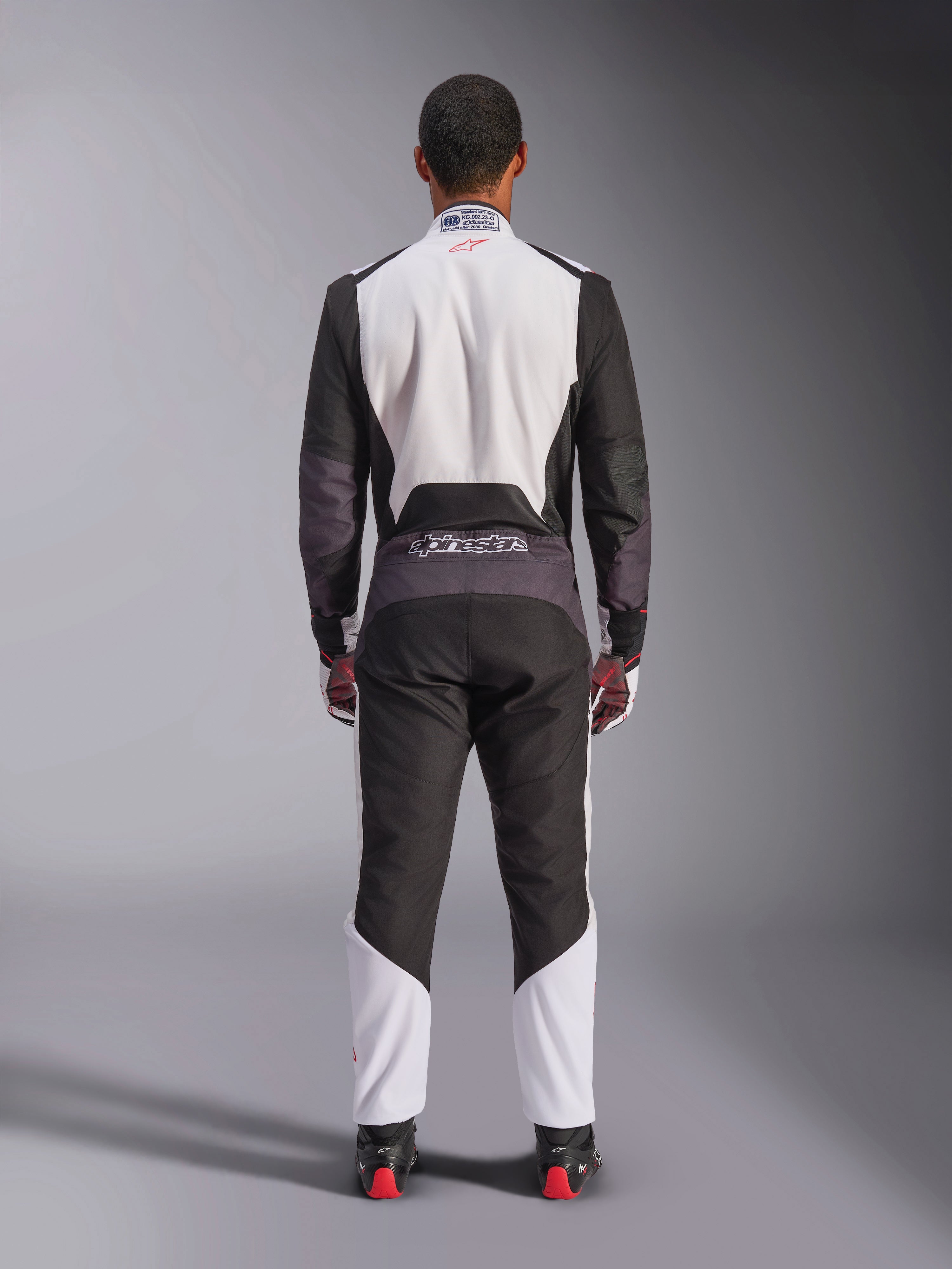 Macacão Alpinestars KMX-5 V3, fato de karting, branco, preto e vermelho vivo, vista traseira, macacão de corrida de uma peça com painéis de malha respirável e logótipo Alpinestars na cintura, usado com luvas e botas de corrida a combinar