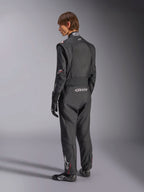 Macacão Alpinestars GP Tech V4, fato de automobilismo, preto com detalhes brancos, vista traseira de modelo a usar o fato com luvas e sapatos de competição, com logótipos brancos na zona lombar e na perna, equipamento de segurança profissional para desportos motorizados