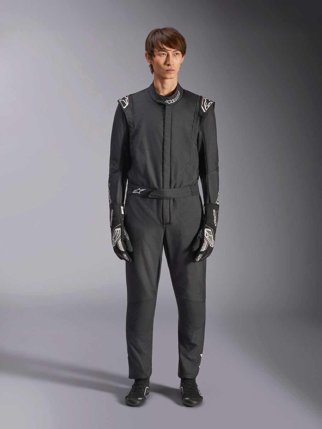 Macacão Alpinestars GP Tech V4, preto e branco, fato profissional de automobilismo de uma só peça, usado com luvas e calçado de competição a condizer, logótipos brancos nos ombros e na gola, corte atlético para competição de desportos motorizados