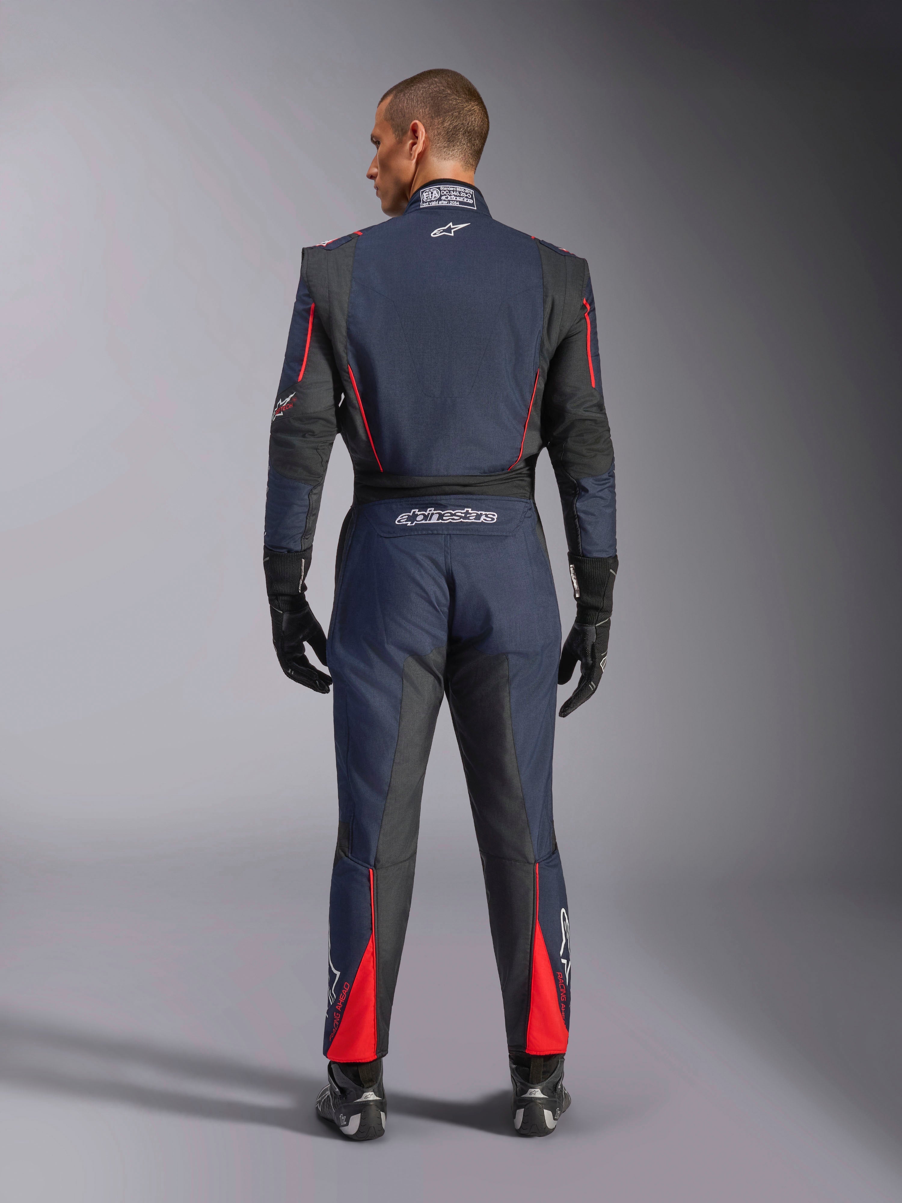 Vista traseira do Macacão Alpinestars GP Tech V4 em Azul Marinho, Preto e Vermelho, macacão de automobilismo de uma peça com painéis elásticos pretos e detalhes vermelhos, com o logótipo Alpinestars e detalhes de certificação FIA, usado com luvas e botas de corrida profissionais