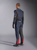 Macacão Alpinestars GP Tech V4, Azul Marinho, Preto e Vermelho, vista lateral traseira de fato de competição automóvel de uma peça, com detalhes em vermelho e painéis pretos, usado com luvas e botas de competição pretas, equipamento de desporto motorizado com certificação FIA