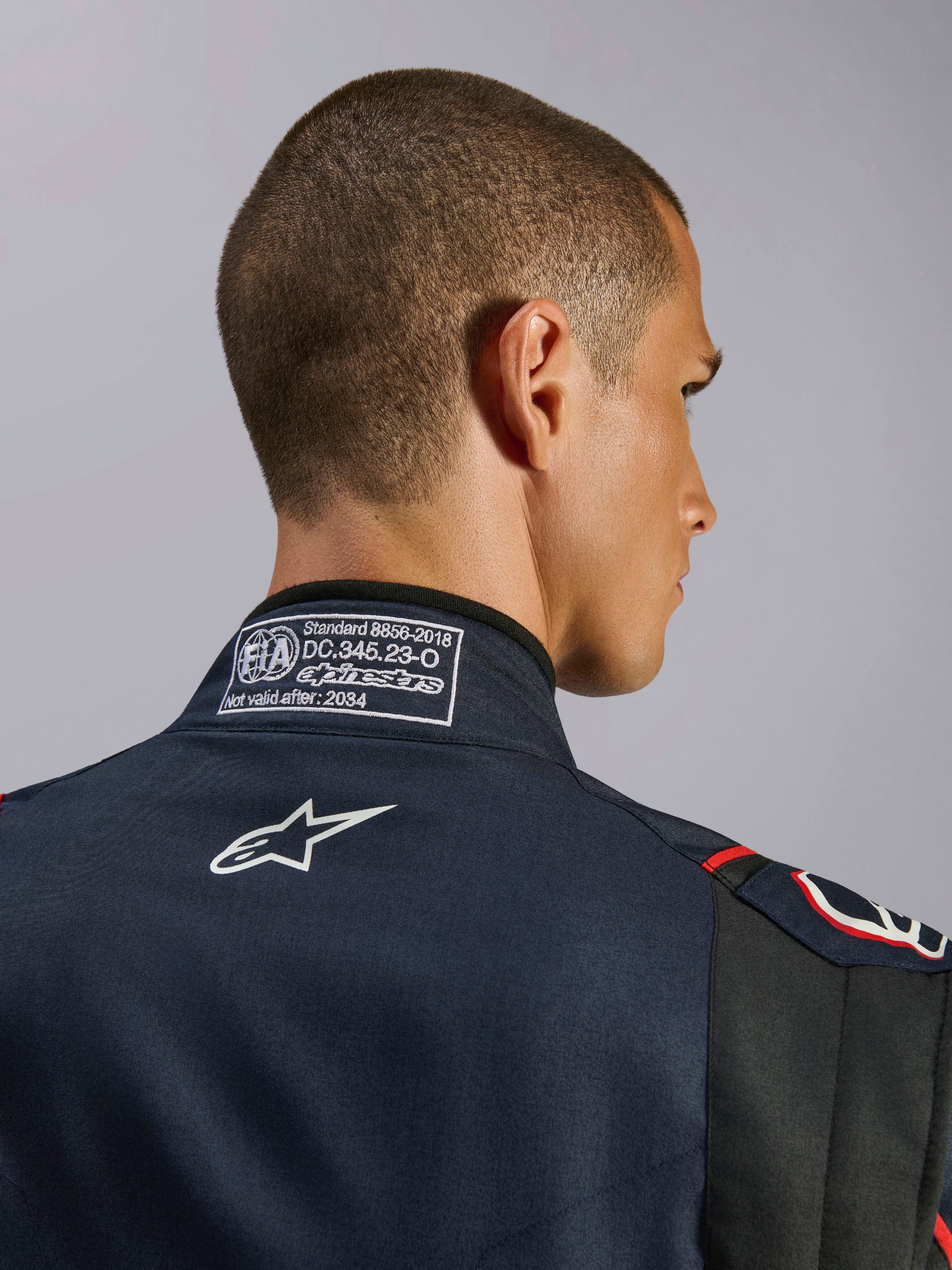 Macacão Alpinestars GP Tech V4 em Azul Marinho, Preto e Vermelho, grande plano da gola traseira com a etiqueta de certificação FIA 8856-2018 e logótipo da Alpinestars bordado a branco, detalhe de macacão de automobilismo de alta performance