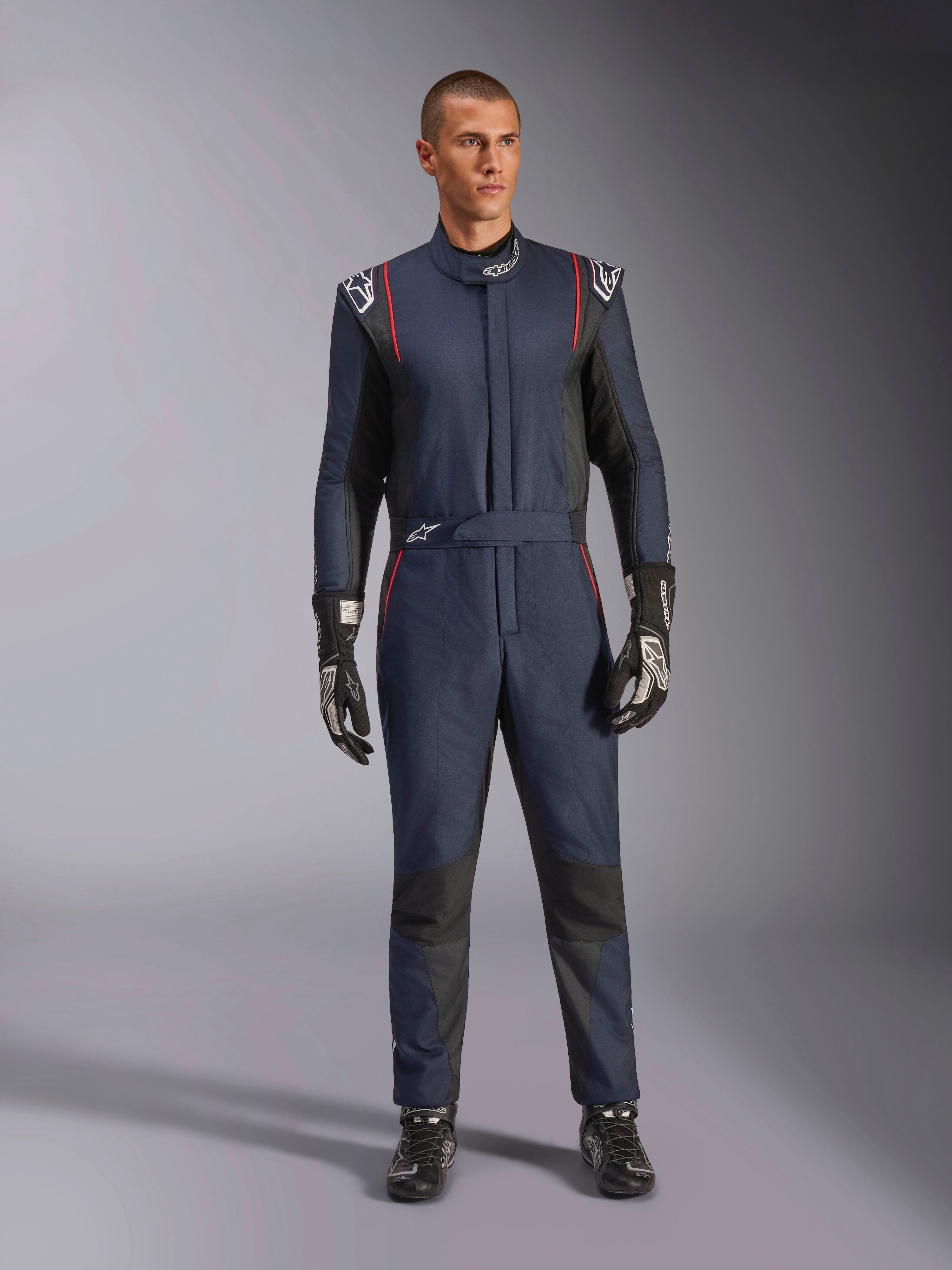 Macacão Alpinestars GP Tech V4, macacão de automobilismo profissional em azul marinho e preto com detalhes em vermelho, equipamento de corrida de peça única com certificação FIA, usado com luvas e calçado de corrida pretos, vestuário para piloto de desportos motorizados