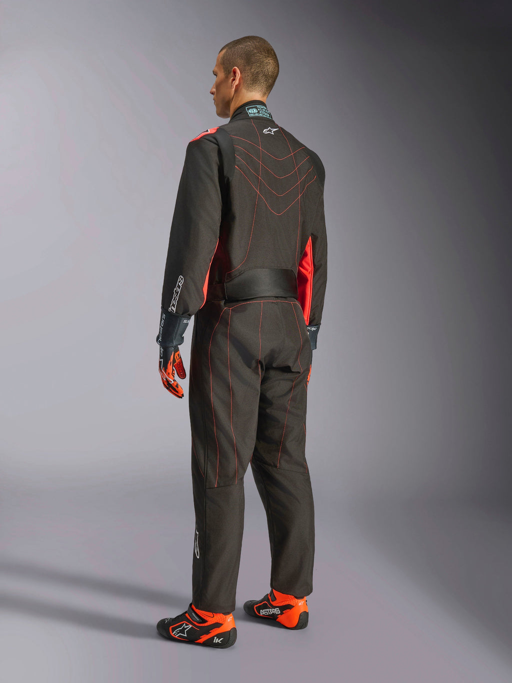 Alpinestars KMX-9 V3 Suit, macacão de karting, preto e vermelho fluorescente, vista traseira, com costuras contrastantes vermelhas e painéis laterais fluorescentes, usado com luvas de corrida e sapatos de karting, vestuário profissional de desportos motorizados