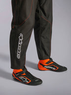 Alpinestars KMX-9 V3 Suit, fato de karting, preto e vermelho fluo, vista detalhada da parte inferior das pernas e botas de corrida, tecido preto com costuras em vermelho fluo, logótipo vertical Alpinestars na perna, combinado com botas de corrida pretas e cor de laranja a condizer, concebido para karting profissional