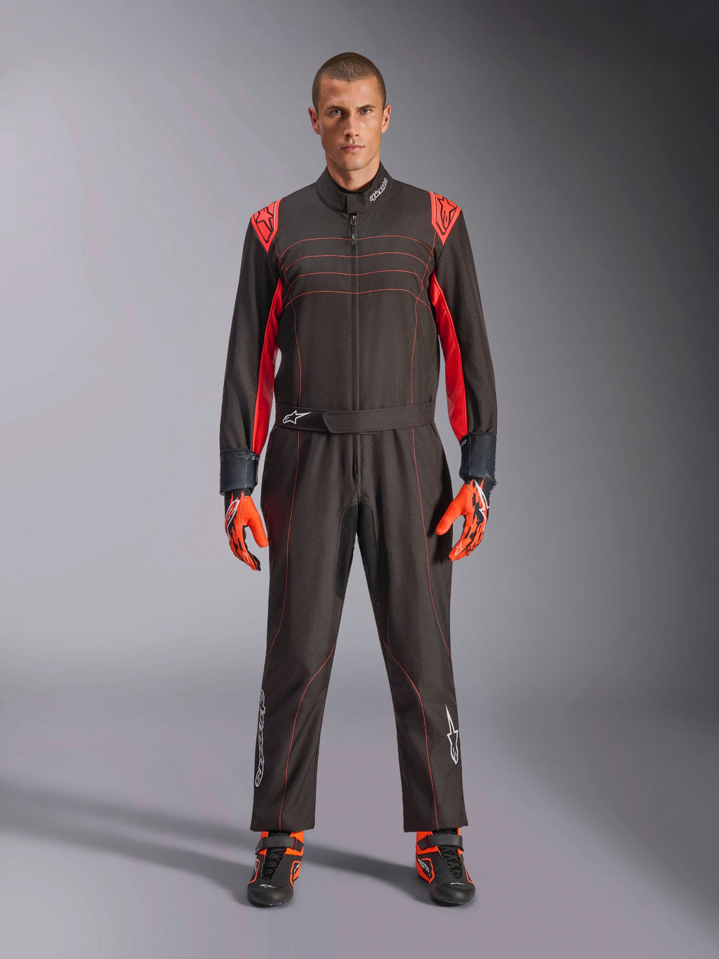 Fato de Karting Alpinestars KMX-9 V3, preto e vermelho fluo, fato de corrida de peça única usado com luvas e botas coordenadas, com pormenores vibrantes nos ombros e costuras a vermelho, logótipo Alpinestars na parte inferior das pernas, design elegante de desporto motorizado para corridas em pista