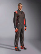 Fato Alpinestars KMX-9 V3, fato de karting, preto e vermelho fluorescente, vestido por um modelo com luvas cor-de-laranja e sapatos de corrida pretos, com costuras vermelhas, detalhes nos ombros e logótipos brancos, design atlético para competição profissional