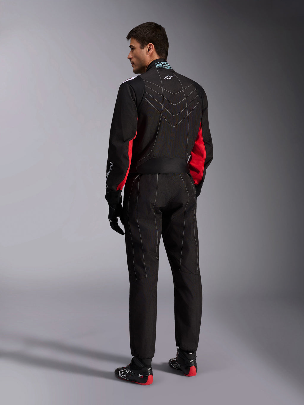 Alpinestars KMX-9 V3 Suit, Black Red White, one-piece karting suit shown from the back, featuring white geometric stitching on the back and red accents on the sleeves, worn with black racing gloves and karting shoes.