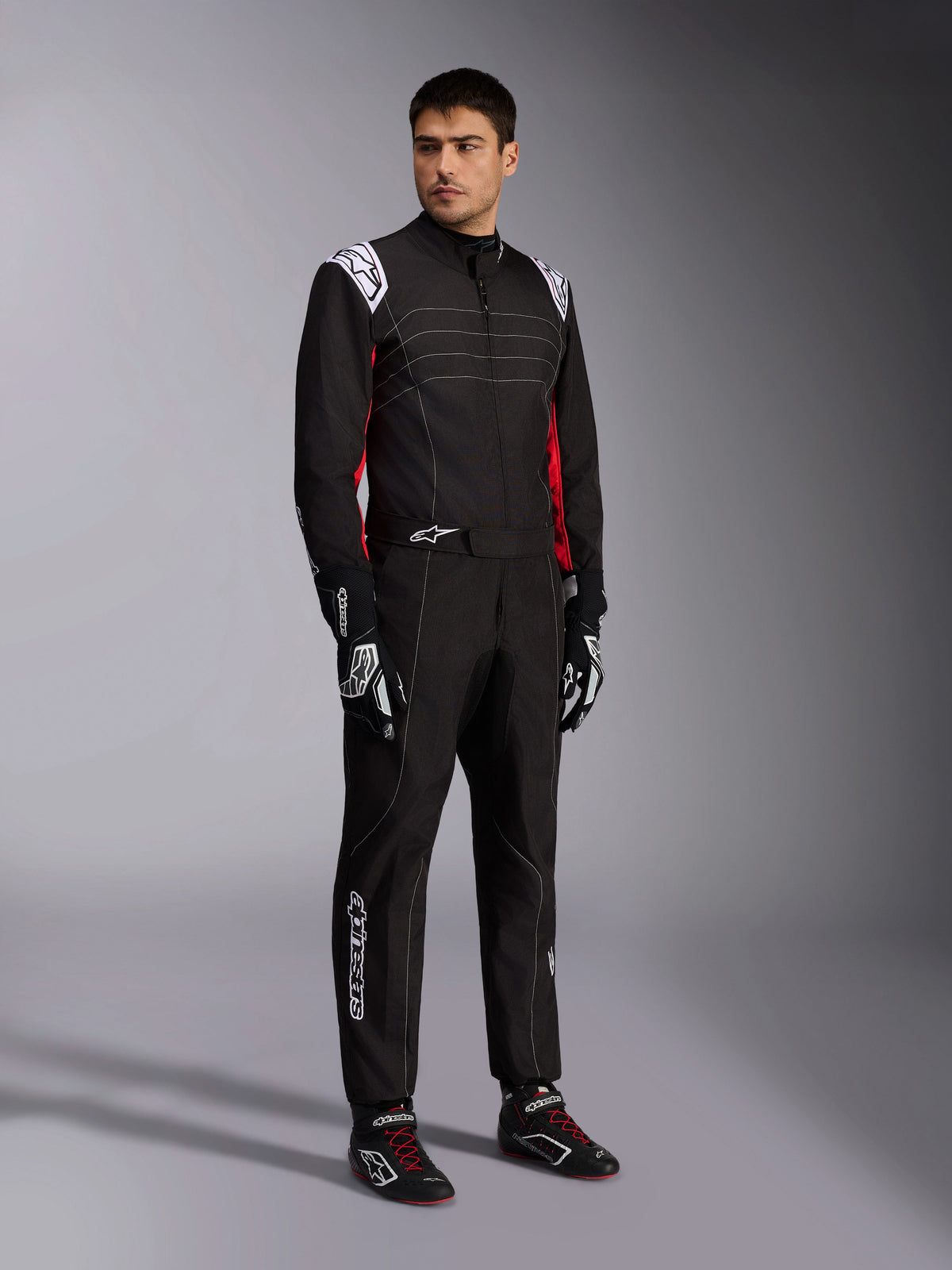 Fato Alpinestars KMX-9 V3, fato de karting em preto, vermelho e branco usado por um modelo, com dragonas e logótipos brancos, detalhes laterais vermelhos, combinado com luvas e sapatos de competição a condizer, vestuário profissional de desportos motorizados