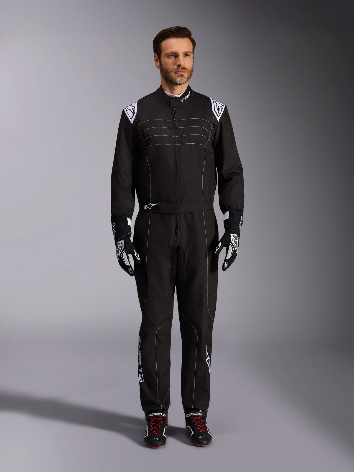 Alpinestars KMX-9 V3 Suit, Black and White Karting Suit, full-length view on a model, featuring white shoulder logos and accents, styled with black and white racing gloves and black shoes with red laces, athletic-regular fit for professional karting gear.