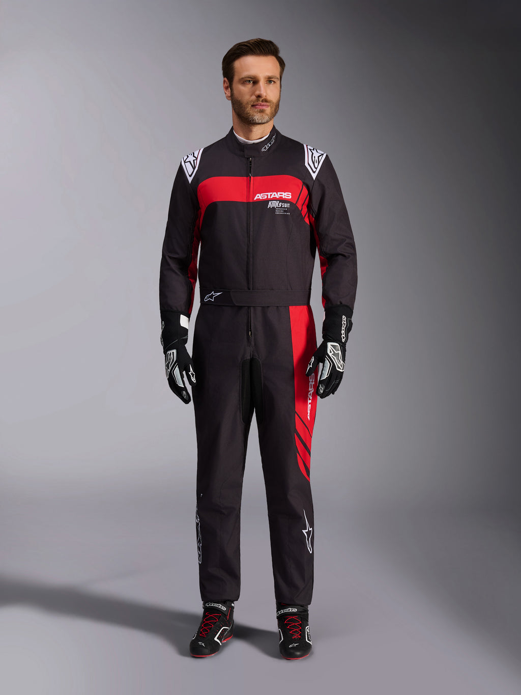 Alpinestars KMX-9 V3 Graphic 3 Suit, fato de karting, preto e vermelho, vista frontal de corpo inteiro usado por um modelo, com painéis gráficos vermelhos arrojados e logótipos brancos, combinado com luvas e sapatilhas de corrida pretas, vestuário profissional de desportos motorizados.