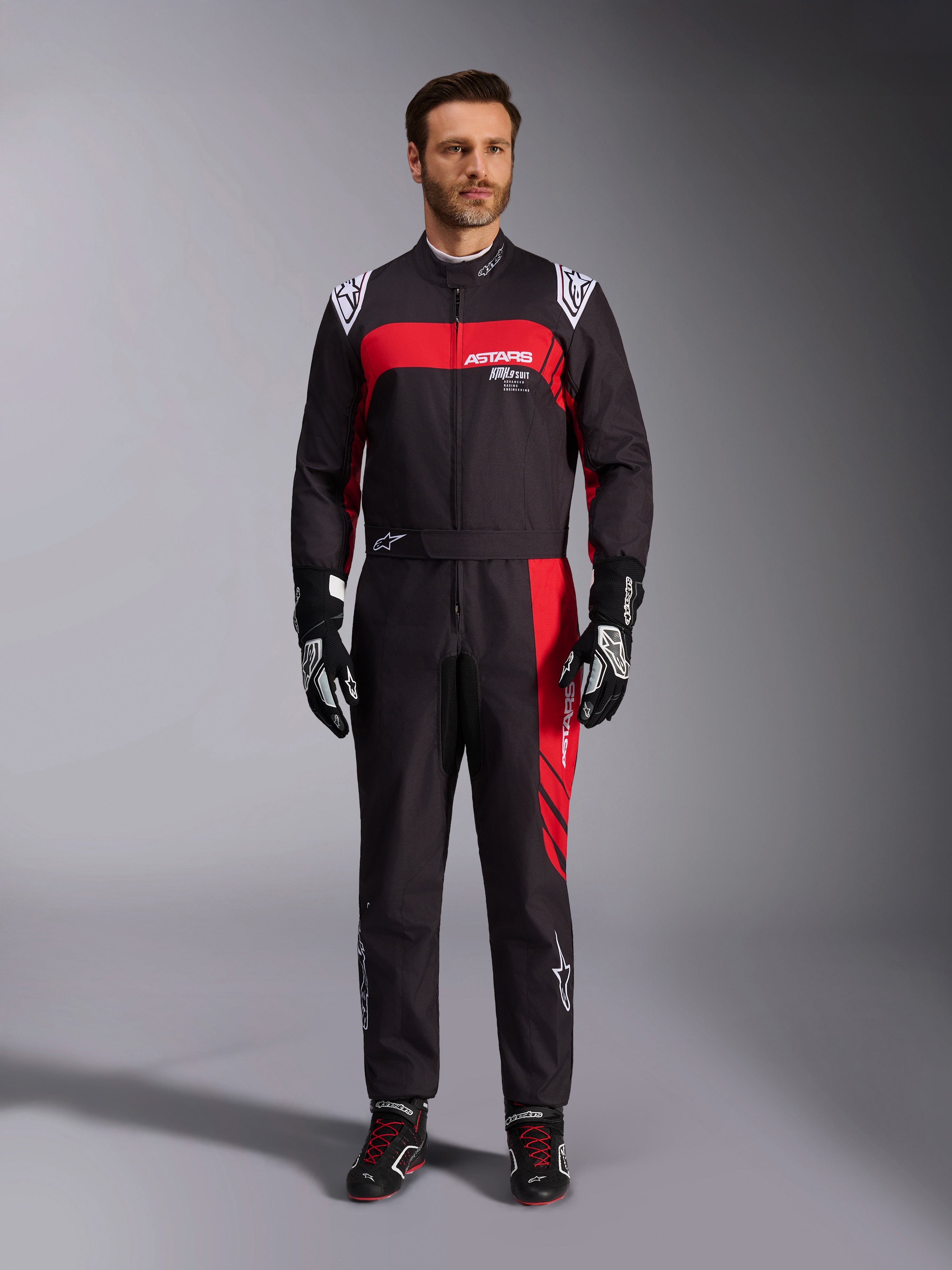 Alpinestars KMX-9 V3 Graphic 3 Suit, fato de karting, preto e vermelho, vista frontal de corpo inteiro usado por um modelo, com painéis gráficos vermelhos arrojados e logótipos brancos, combinado com luvas e sapatilhas de corrida pretas, vestuário profissional de desportos motorizados.