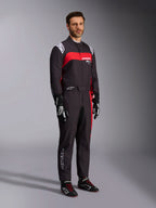 Modelo masculino a usar o fato Alpinestars KMX-9 V3 Graphic 3, fato de karting, preto e vermelho, com dragonas brancas nos ombros e logótipo vermelho no peito, combinado com luvas de corrida pretas e sapatos com atacadores vermelhos, vestuário profissional de desporto motorizado