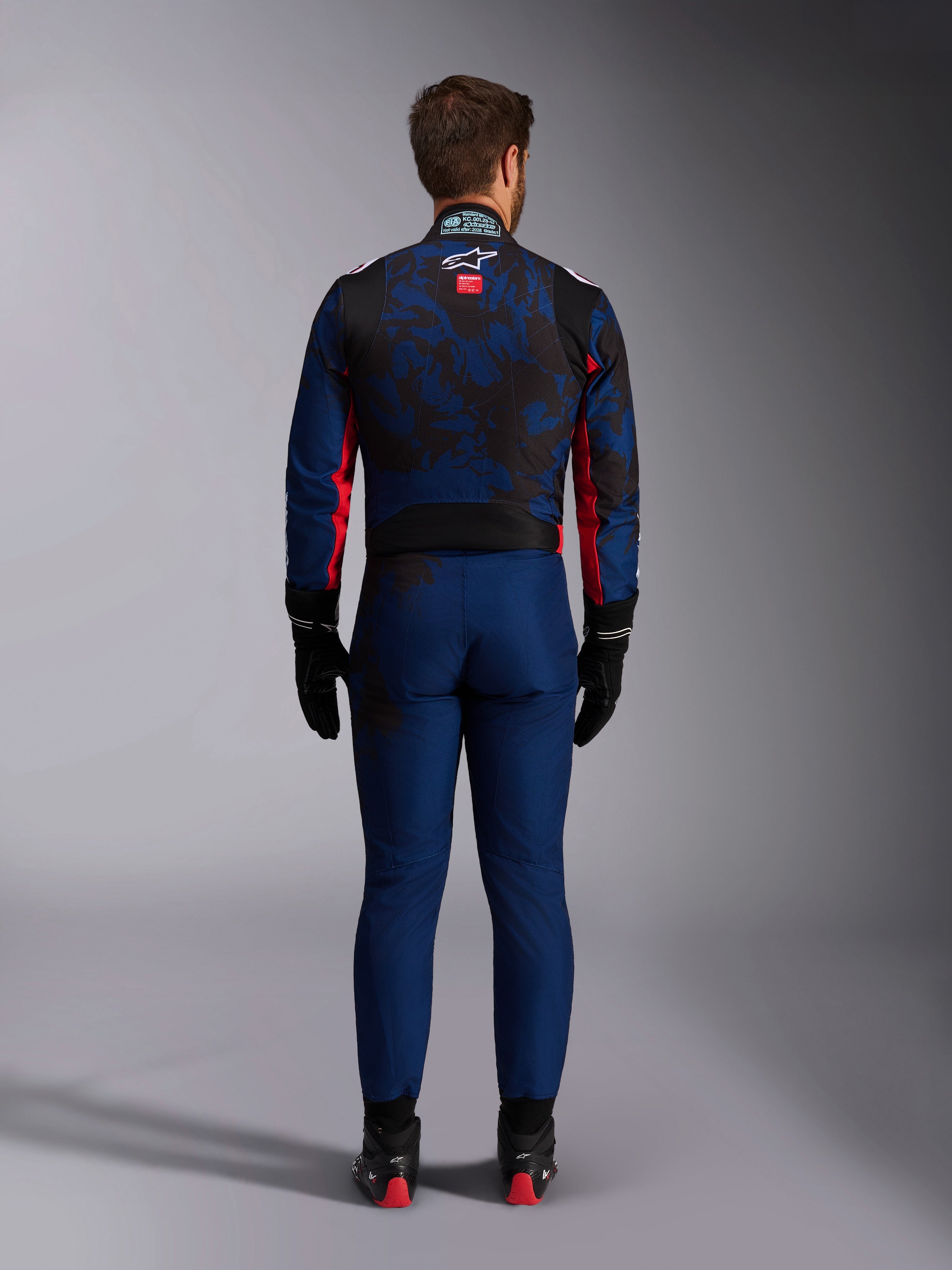 Karting driver from the back wearing the KMX-9 V3 Graphic 5 Suit in Navy Red, featuring a navy blue and black graphic pattern, red side accents, and the Alpinestars logo on the upper back, paired with black racing gloves and footwear.