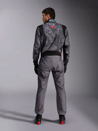 Macacão Alpinestars KMX-9 V3 Graphic 5, fato de karting, padrão de camuflagem cinzento escuro e preto na parte superior, vista traseira com painéis elásticos e logótipos Alpinestars, usado com luvas pretas e sapatos de corrida pretos com detalhes vermelhos, equipamento profissional de desporto motorizado