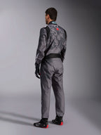 Alpinestars KMX-9 V3 Graphic 5 Suit, macacão de karting cinzento escuro e preto, vista traseira de modelo a usar equipamento de corrida completo, incluindo luvas pretas e vermelhas e sapatos de karting, com padrões gráficos integrados e logótipo nas costas.