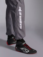Macacão Alpinestars KMX-9 V3 Graphic 5, fato de karting, cinzento escuro, pormenor da parte inferior da perna com logótipo vertical Alpinestars em branco, usado com botas de corrida pretas e vermelhas, material durável para competição de karting