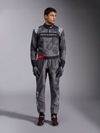 Macacão Alpinestars KMX-9 V3 Graphic 5, fato de karting, cinzento escuro e preto com grafismos estilo camuflagem, com uma faixa preta no peito com logótipo branco e um detalhe de cinto vermelho na cintura, usado com luvas e sapatos de corrida a condizer, equipamento profissional de desportos motorizados