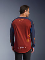 Alpinestars Maxdura Dual Jersey em castanho ferrugem e Mood Indigo, vista de costas, com torso em malha respirável, mangas azul-escuro com branding Alpinestars em cor de laranja e bainha traseira descaída para maior cobertura.