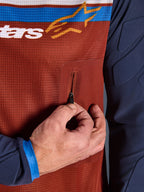 Primeiro plano da Alpinestars Maxdura Dual Jersey, torso em malha Rust Brown com bolso no peito com fecho de correr sem costuras, mangas Mood Indigo com acolchoamento integrado, pormenor de camisola técnica de motociclismo de aventura