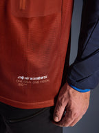 Alpinestars Maxdura Dual Jersey, camisola de motociclismo de aventura, castanho ferrugem e azul Mood Indigo, vista em pormenor do tecido em malha do tronco e da manga tecida em azul-marinho, logótipo Alpinestars 'One Goal One Vision' a branco na bainha inferior.