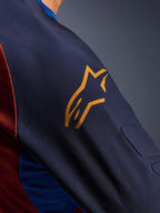 Alpinestars Maxdura Dual Jersey, grande plano da manga Mood Indigo com um logótipo amarelo da Alpinestars, mostrando o acolchoamento integrado em malha espaçadora e o tecido do tronco em malha Rust Brown, vestuário técnico de motociclismo de aventura