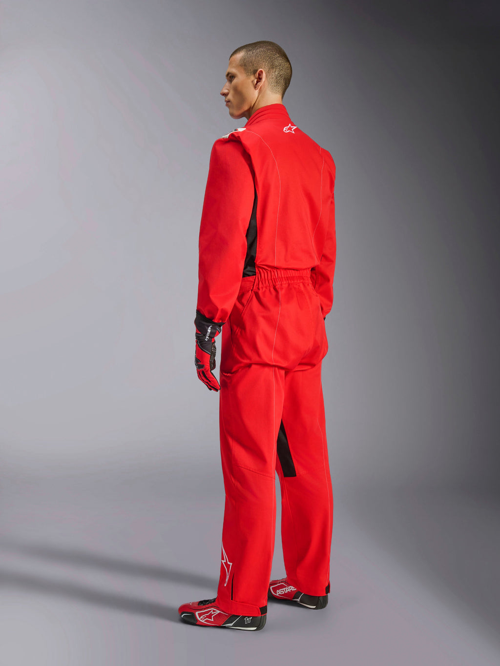 Fato Alpinestars Kart Indoor V2, fato de karting vermelho, vista traseira de três quartos num modelo, usado com luvas vermelhas e botas de competição a condizer, construção de sarja de camada única em poli-algodão, equipamento profissional para karting indoor