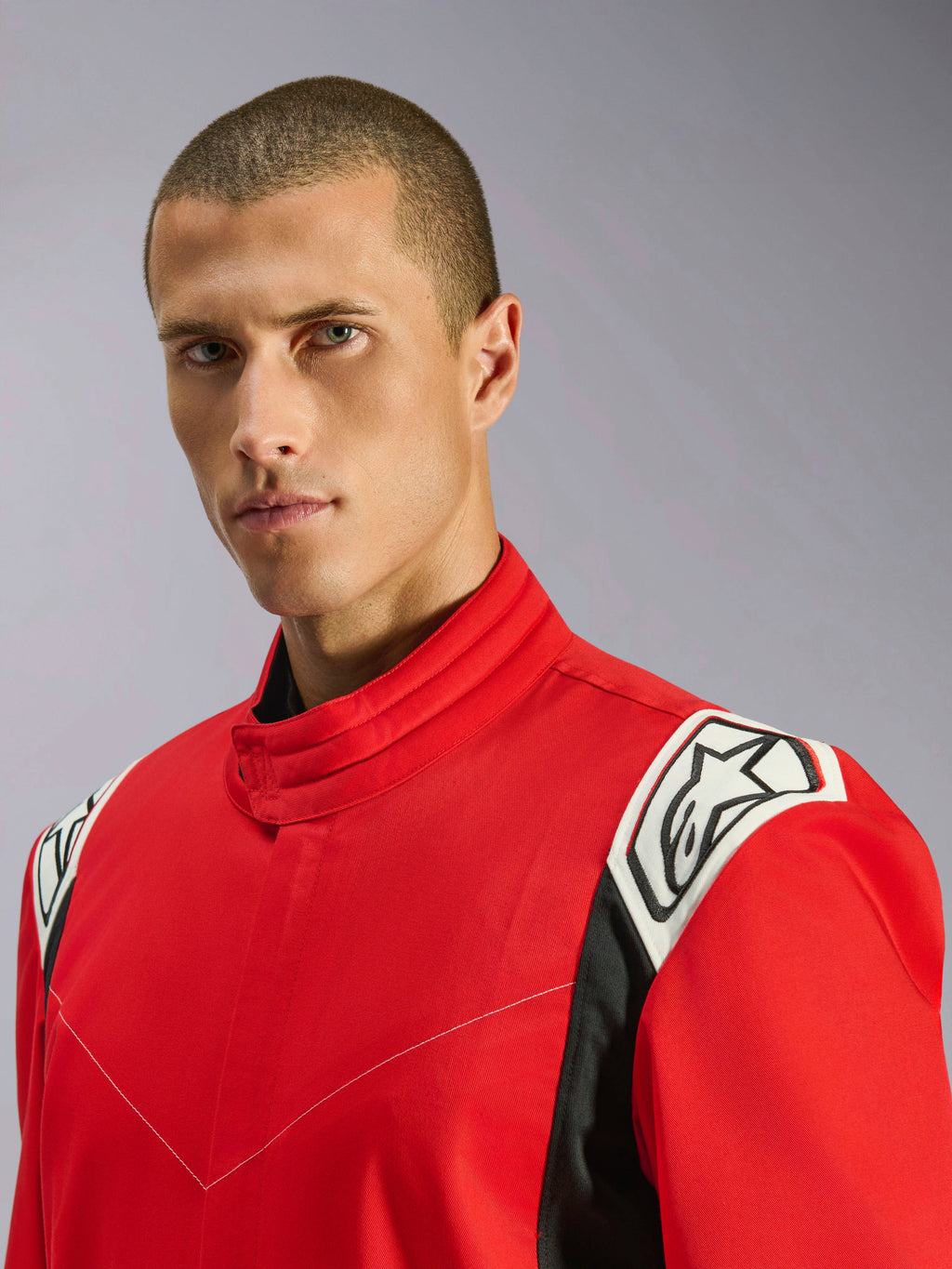 Fato Alpinestars Kart Indoor V2 em vermelho, retrato em grande plano de um modelo masculino a usar o fato, destacando a gola ergonómica e os detalhes nos ombros em branco e preto com o logótipo Alpinestars