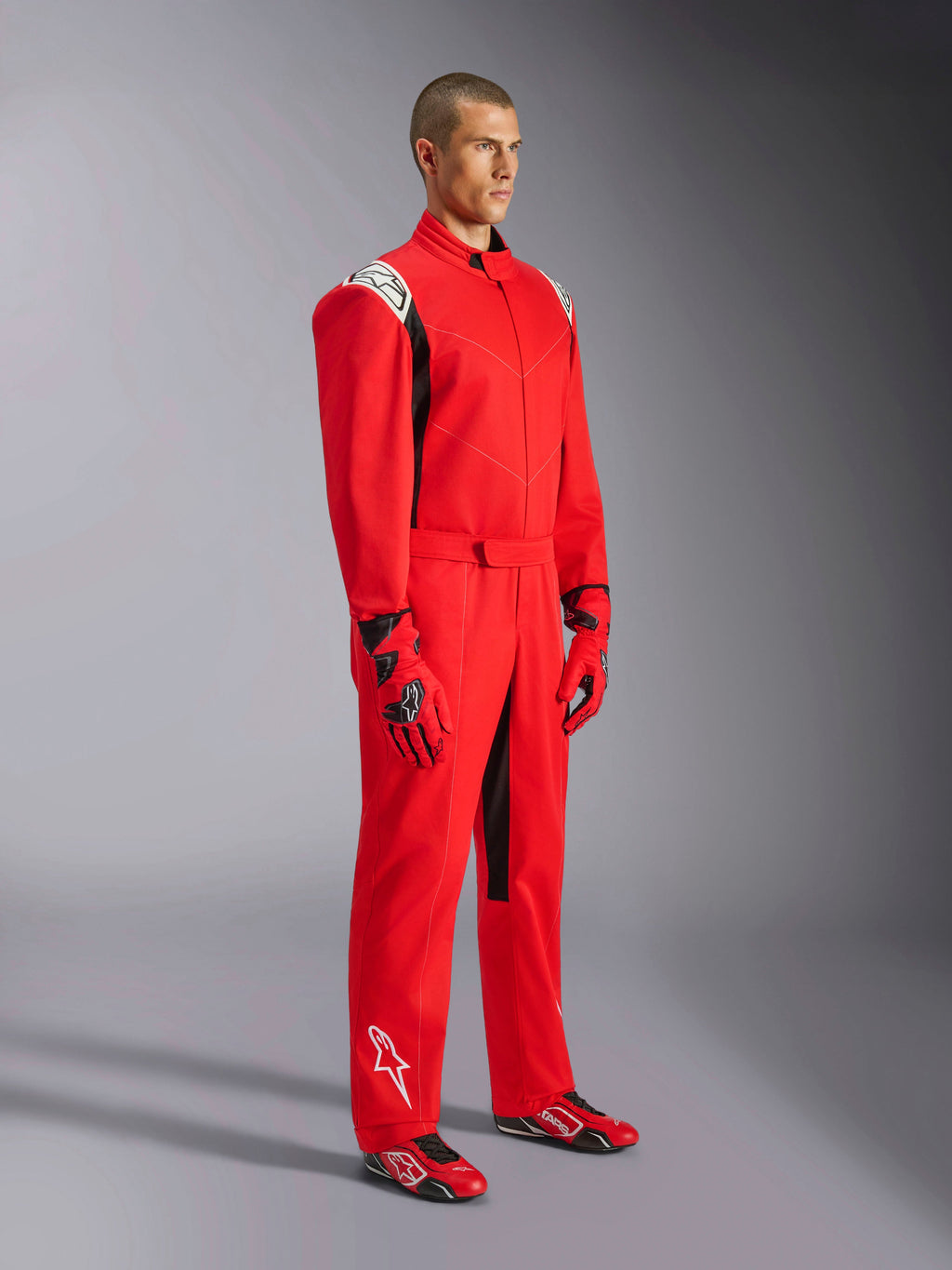 Fato Alpinestars Kart Indoor V2, macacão de karting vermelho, usado por um modelo com luvas e sapatos vermelhos e pretos a condizer, com logótipos brancos nos ombros e na parte inferior da perna, detalhes pretos, concebido para karting recreativo e pistas indoor