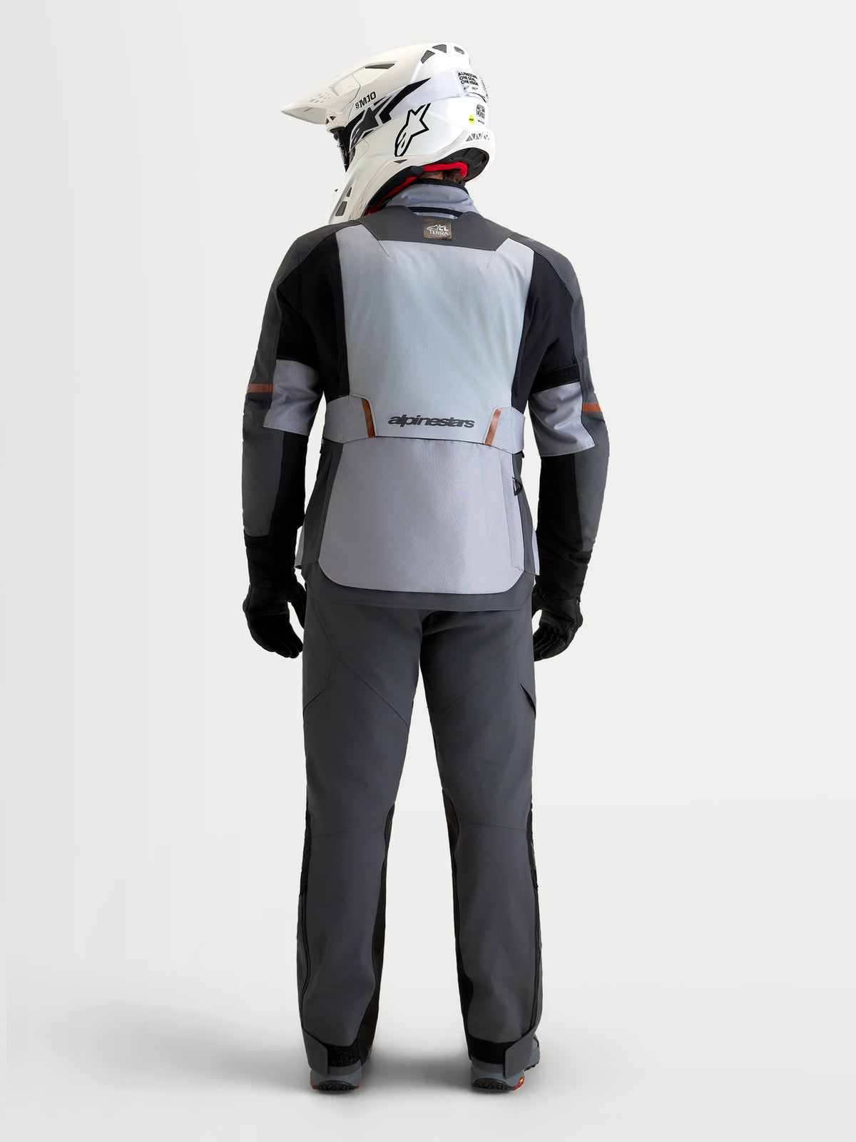 Alpinestars St-7 V2 2L Gore-Tex Gear Set, adventure touring motorcycle jacket and pants in mid gray, deep gray, and black, rear profile view of a model wearing matching waterproof textile riding gear and helmet