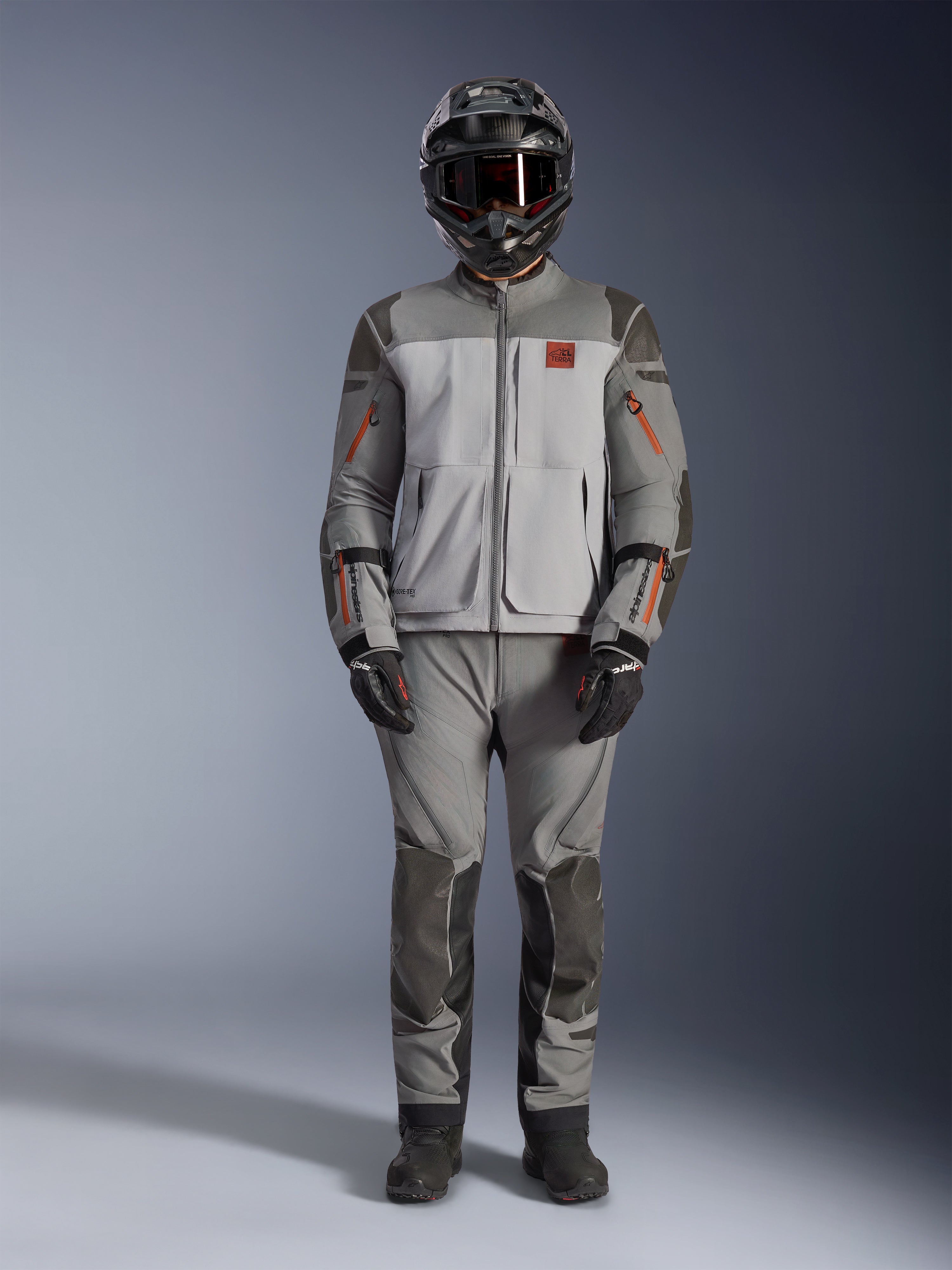 Alpinestars Nazca 3L GORE-TEX PRO Jacket, Adventure Motorcycle Jacket, Dark Gray and Mid Gray with orange accents, featuring Superfabric reinforcements and front ventilation zips, worn with matching pants and black helmet, technical all-terrain riding gear