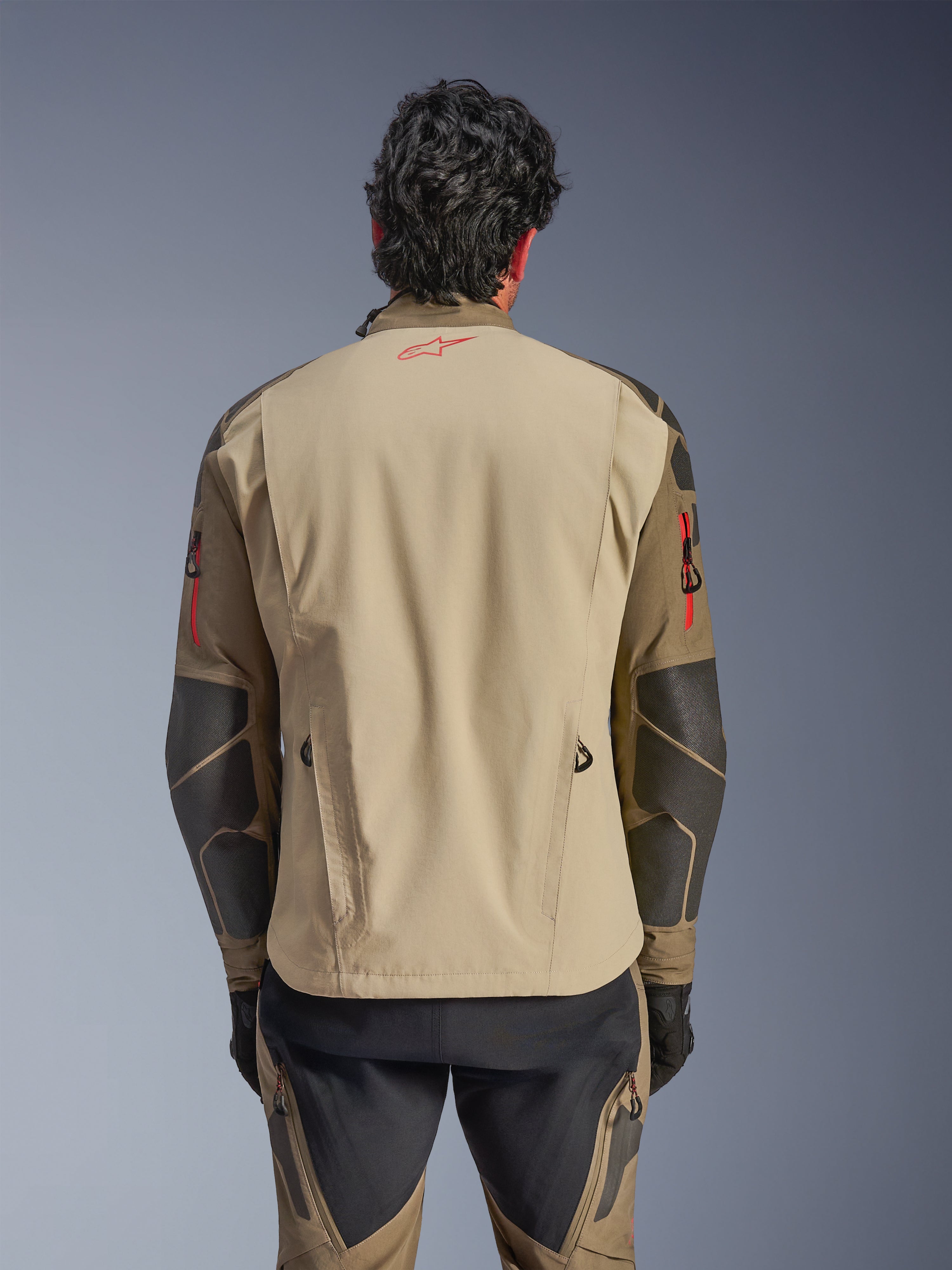 Casaco Alpinestars Nazca 3L GORE-TEX PRO, vista traseira, Walnut Rock Brown, casaco de motociclismo de aventura com logótipo Astars vermelho na gola e detalhes de fechos vermelhos nos braços, com reforços Superfabric nos cotovelos.