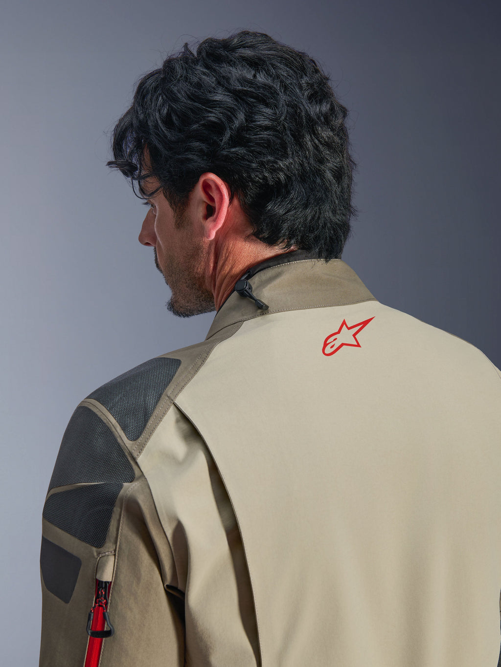 Casaco Alpinestars Nazca 3L GORE-TEX PRO, casaco de aventura em castanho Walnut Rock Brown, grande plano das costas e do ombro, logótipo de estrela vermelha na gola, painéis de reforço texturizados cinzentos, construção têxtil durável para motociclismo