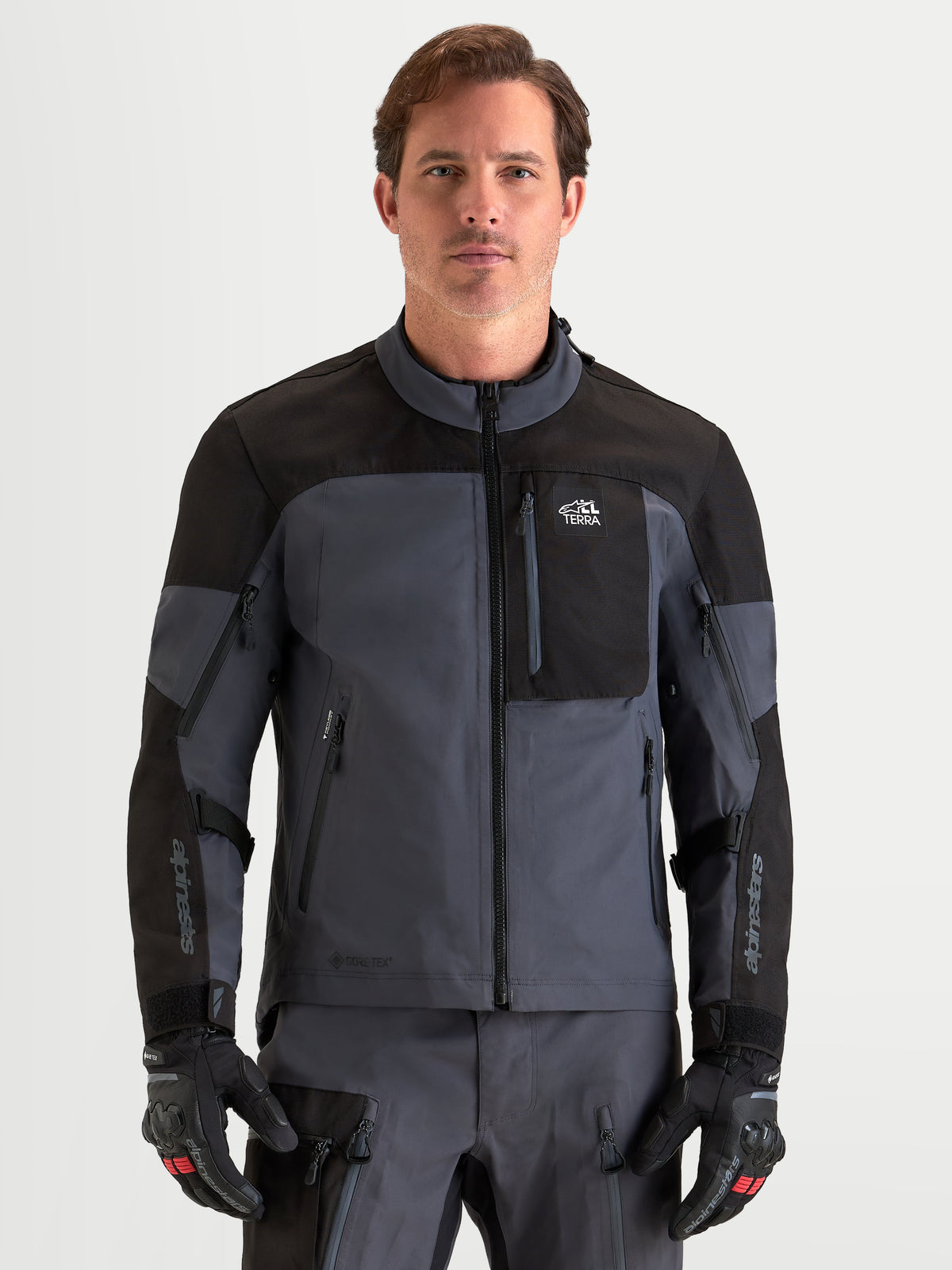 Alpinestars Arenis Gore-Tex casaco de moto para homem, em preto e cinzento escuro, vista frontal num modelo a usar equipamento e luvas a condizer, vestuário de turismo todo-o-terreno impermeável certificado AA