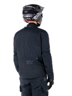 Alpinestars St-7 Prime GORE-TEX Jacket, Black, rear view of a rider wearing the jacket with a matching helmet and pants, featuring Alpinestars branding and geographic coordinates on the lower back.