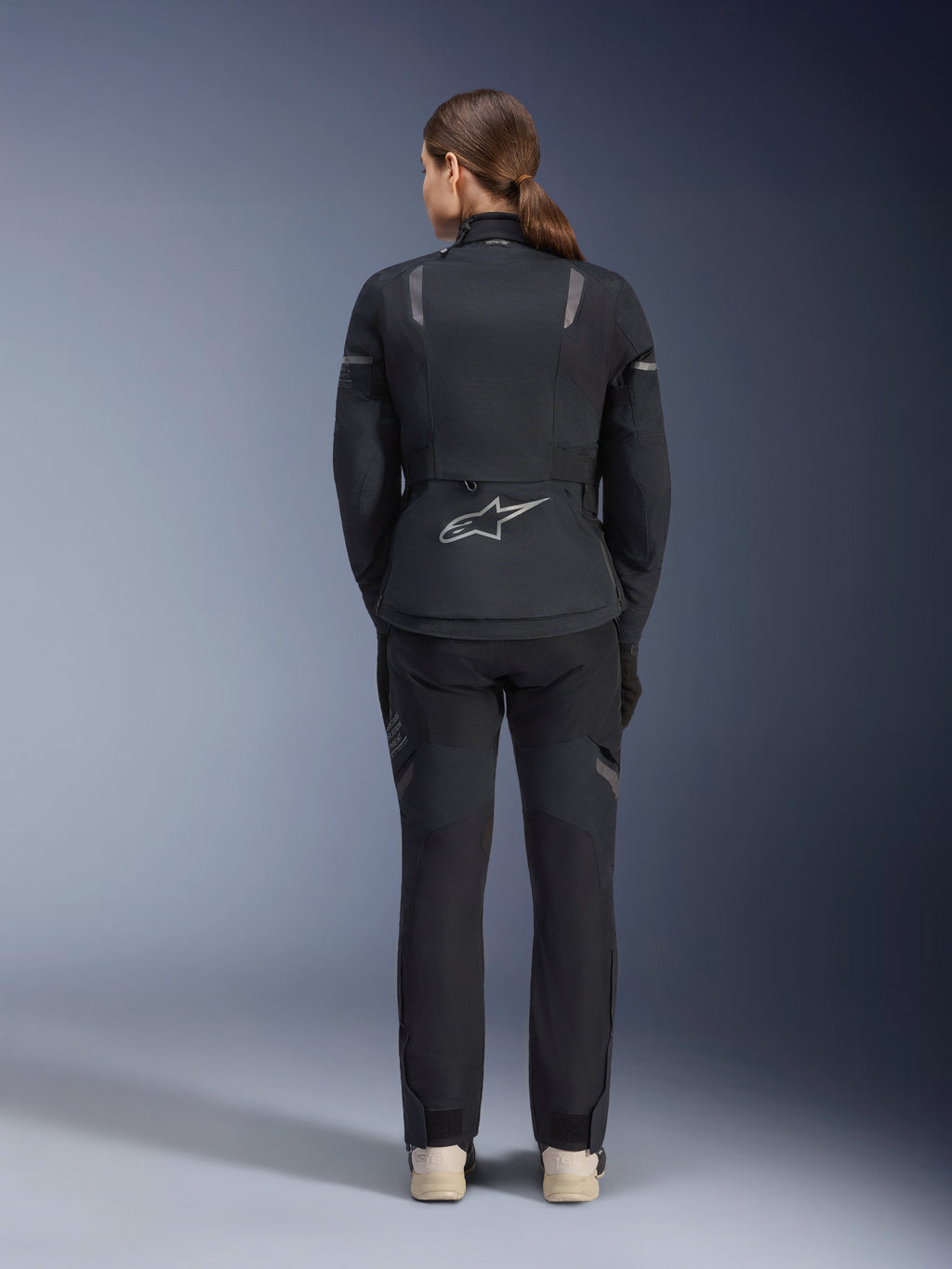 Casaco Alpinestars Stella ST-7 2L GORE-TEX Feminino, preto e cinzento escuro, vista traseira com o logótipo prateado da Alpinestars na parte inferior das costas, combinado com calças têxteis pretas a condizer, equipamento de motociclismo adventure touring