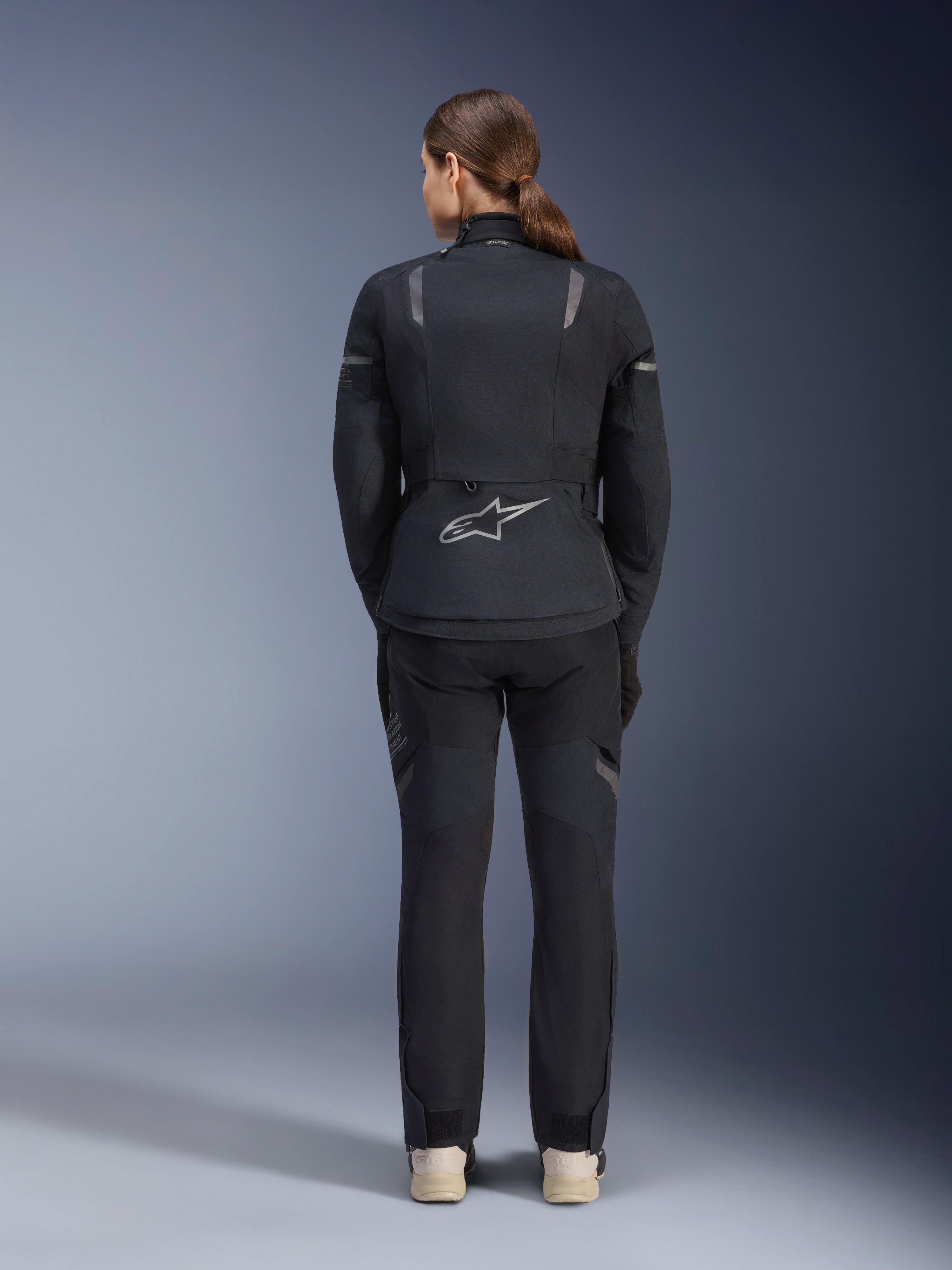 Casaco Alpinestars Stella ST-7 2L GORE-TEX Feminino, preto e cinzento escuro, vista traseira com o logótipo prateado da Alpinestars na parte inferior das costas, combinado com calças têxteis pretas a condizer, equipamento de motociclismo adventure touring