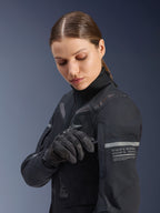 Casaco Alpinestars Stella ST-7 2L GORE-TEX Feminino, casaco de aventura e turismo de estrada, preto e cinzento escuro, usado por uma mulher a ajustar um pormenor na manga, com tiras refletoras e gráficos de coordenadas, camada têxtil durável para todas as estações